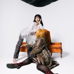 Two women in stylish outfits pose in a modern studio setting with vibrant armchair.