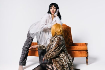 Two women in stylish outfits pose in a modern studio setting with vibrant armchair.