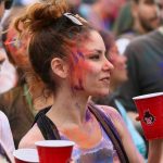 People enjoying a vibrant celebration with colorful face paints and drinks in New York.