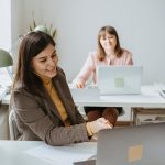Two women working together with laptops in a bright and modern office setting.