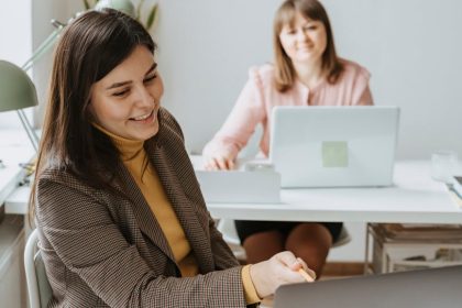 Two women working together with laptops in a bright and modern office setting.