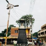 Street view of a bust sculpture in an Indian town square, surrounded by buildings and people.