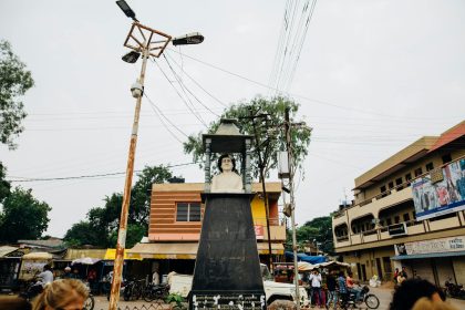 Street view of a bust sculpture in an Indian town square, surrounded by buildings and people.