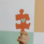 A hand holds a red puzzle piece with a heart, symbolizing connection and awareness.