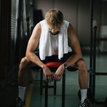 A young man with a towel takes a break in the gym, reflecting on his workout.
