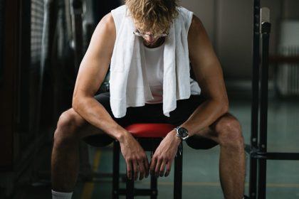A young man with a towel takes a break in the gym, reflecting on his workout.