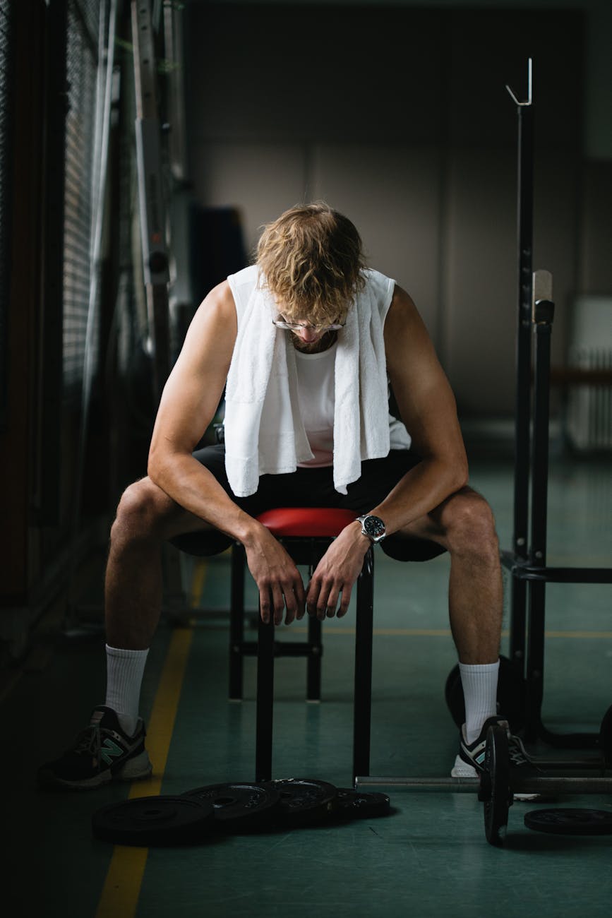 A young man with a towel takes a break in the gym, reflecting on his workout.