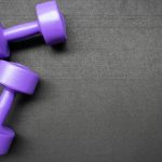 Pair of purple dumbbells on a dark gray background, perfect for fitness themes.