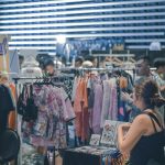 Vibrant indoor clothing market scene with diverse shoppers browsing and buying fashionable apparel.