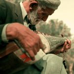 Elderly man outdoors playing a traditional instrument in Islamabad, Pakistan, showcasing cultural heritage.