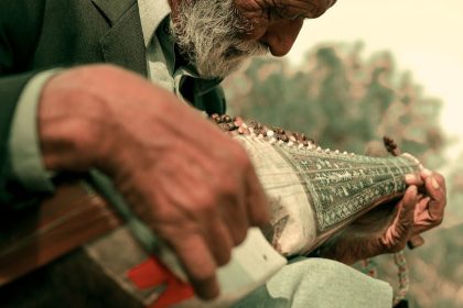 Elderly man outdoors playing a traditional instrument in Islamabad, Pakistan, showcasing cultural heritage.