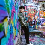 A stylish young man leans against a vibrantly painted graffiti wall.