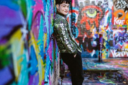 A stylish young man leans against a vibrantly painted graffiti wall.