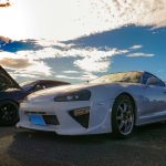 Captivating photo of JDM culture featuring a Toyota Supra at a vibrant car meet under a stunning sky.