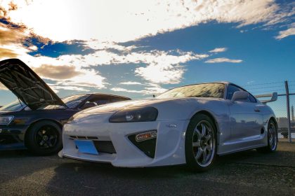 Captivating photo of JDM culture featuring a Toyota Supra at a vibrant car meet under a stunning sky.