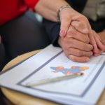Two adults holding hands over business documents, symbolizing support and partnership.