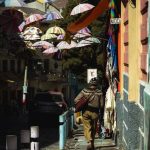 Vibrant umbrellas hang above a city sidewalk, creating a colorful street decoration scene.