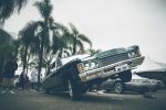 A vibrant lowrider car with palm trees and people at an outdoor car show.