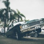 A vibrant lowrider car with palm trees and people at an outdoor car show.