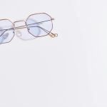 Close-up of hexagonal eyeglasses with blue tint on a white background, minimalistic style.