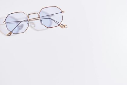 Close-up of hexagonal eyeglasses with blue tint on a white background, minimalistic style.