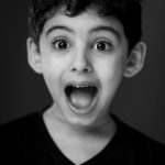 A monochrome portrait of a surprised young boy with wide eyes and open mouth.