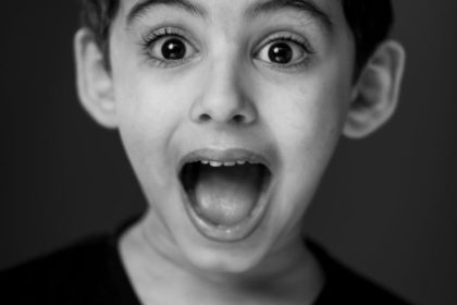 A monochrome portrait of a surprised young boy with wide eyes and open mouth.