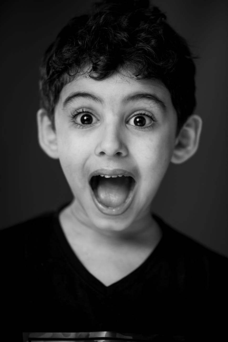 A monochrome portrait of a surprised young boy with wide eyes and open mouth.