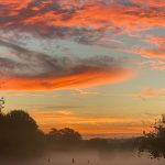 Vivid autumn sunrise with orange clouds over a misty golf course in Sheffield, UK.