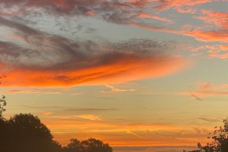 Vivid autumn sunrise with orange clouds over a misty golf course in Sheffield, UK.