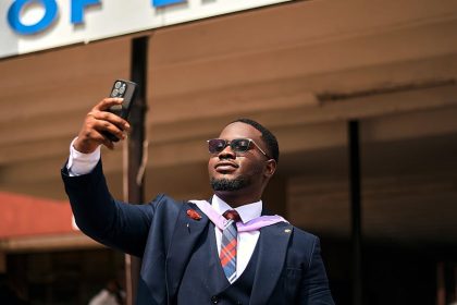 Proud graduate taking a selfie outside engineering building with sign.