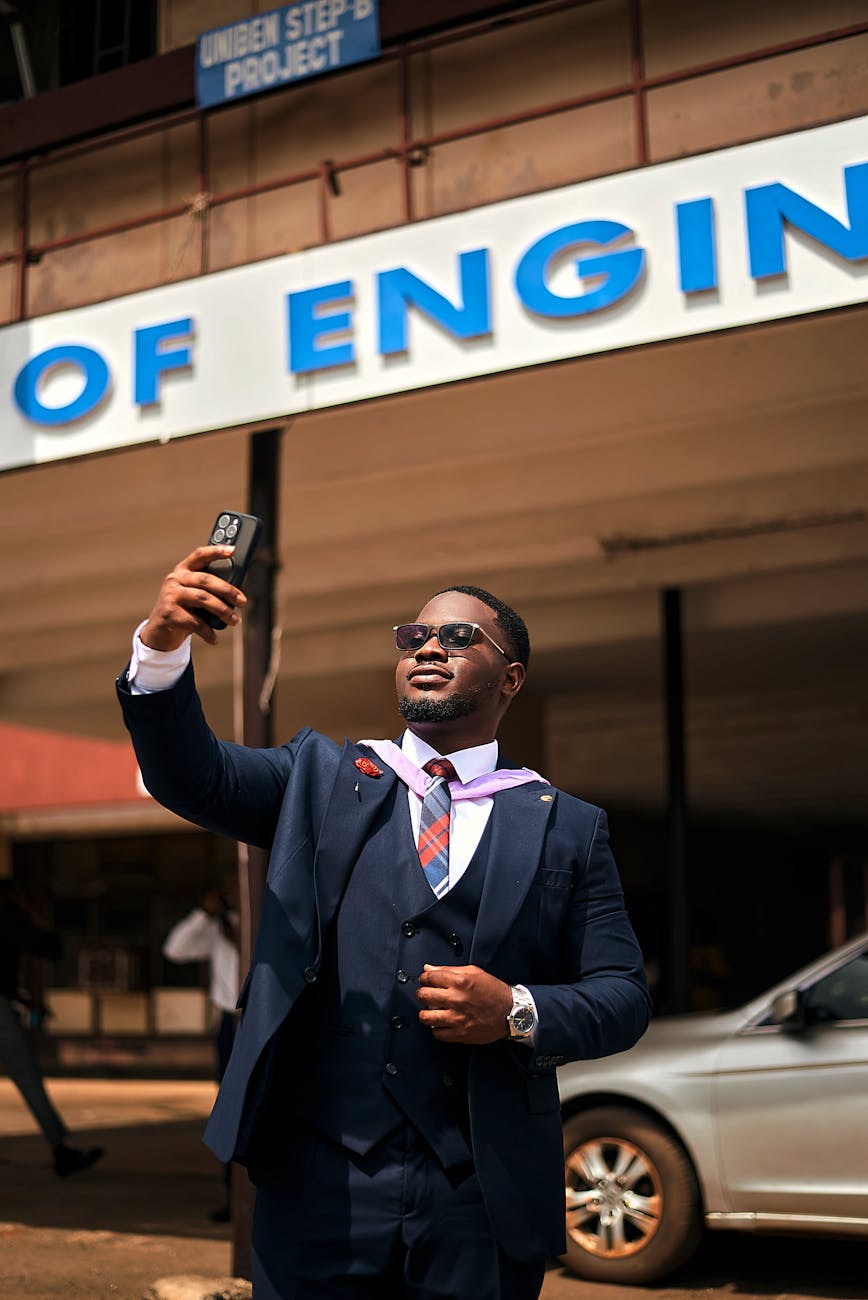 Proud graduate taking a selfie outside engineering building with sign.