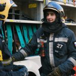Two firefighters in full gear discussing strategies next to a fire truck.