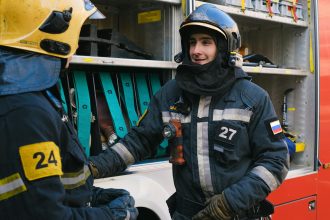 Two firefighters in full gear discussing strategies next to a fire truck.