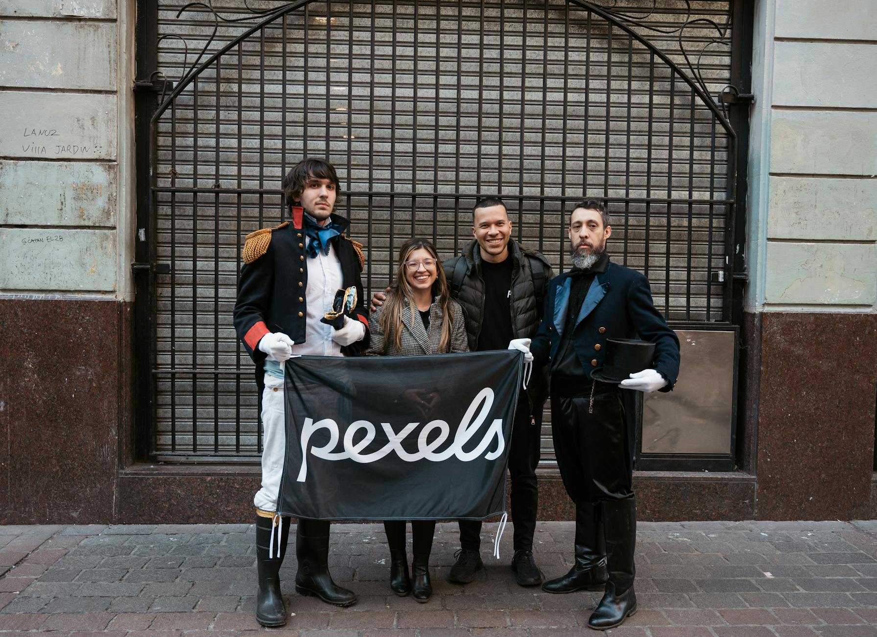 People posing with a Pexels banner in Buenos Aires, featuring historical costumes.
