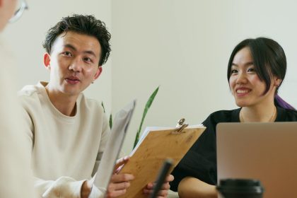 Two colleagues brainstorming at a workplace with laptops, papers, and smiles.