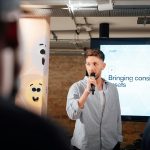 Man presenting with microphone at a business event in London, engaging audience.