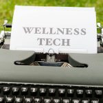 A retro typewriter outdoors displaying a 'Wellness Tech' message on paper.