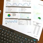 Flatlay of a business analytics report, keyboard, pen, and smartphone on a wooden desk.